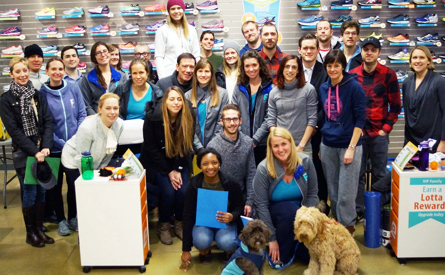 A group of smiling staff and volunteers posing for a photo in front of a wall of shoes.