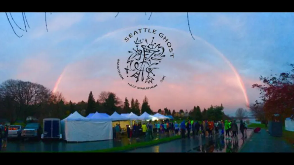 Runners gathered under a rainbow at the Seattle Ghost Marathon event, with the race logo visible in the sky.