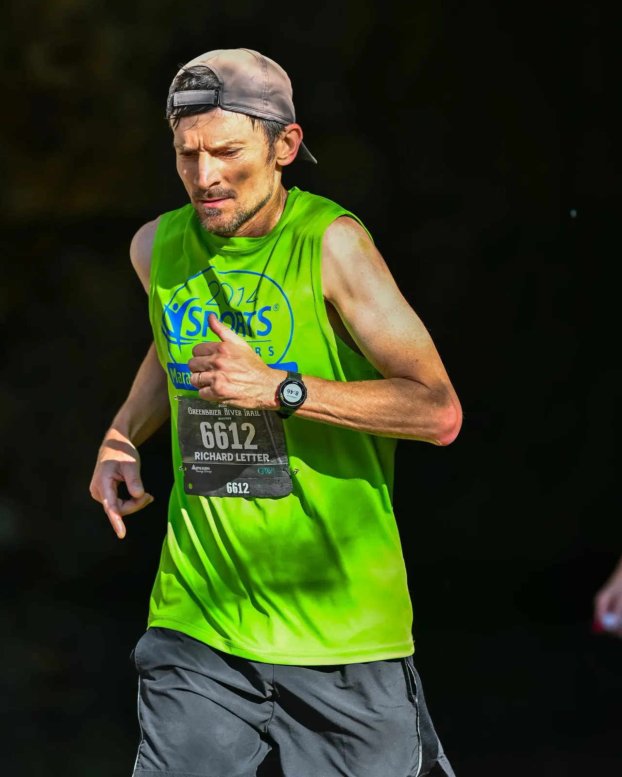 A male runner with a green sleeveless shirt and black shorts running on a trail, wearing a bib with the number 6612.