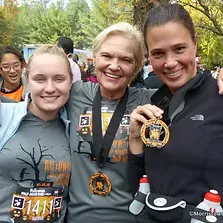 Three smiling women pose for a photo, two of them wearing race medals.