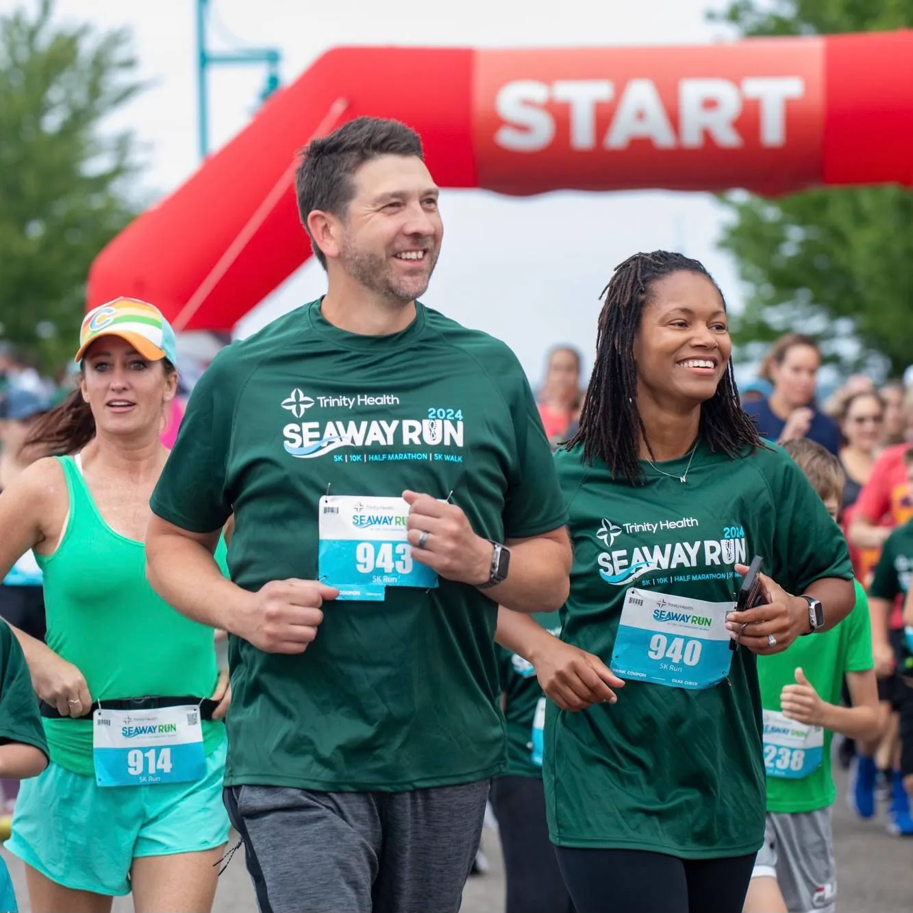 Three runners smiling as they cross the start line at the Trinity Health Seaway Run.