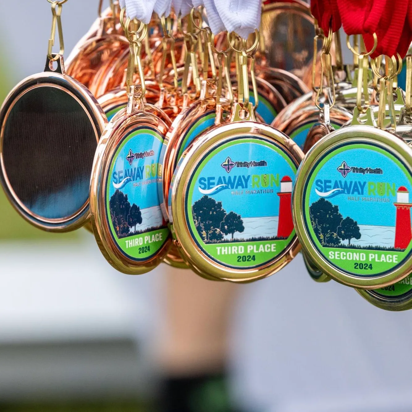 A close-up shot of several Seaway Run Half Marathon medals hanging from ribbons, showing the race logo and lighthouse design.