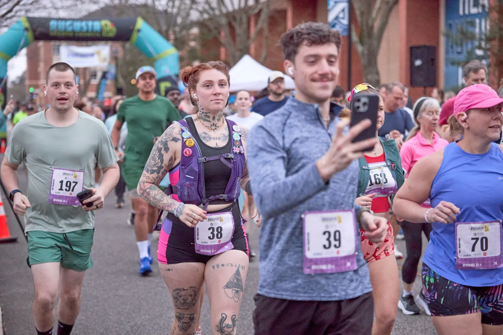 Runners crossing the start line at the Augusta Half Marathon, with bib numbers visible and the race arch in the background.