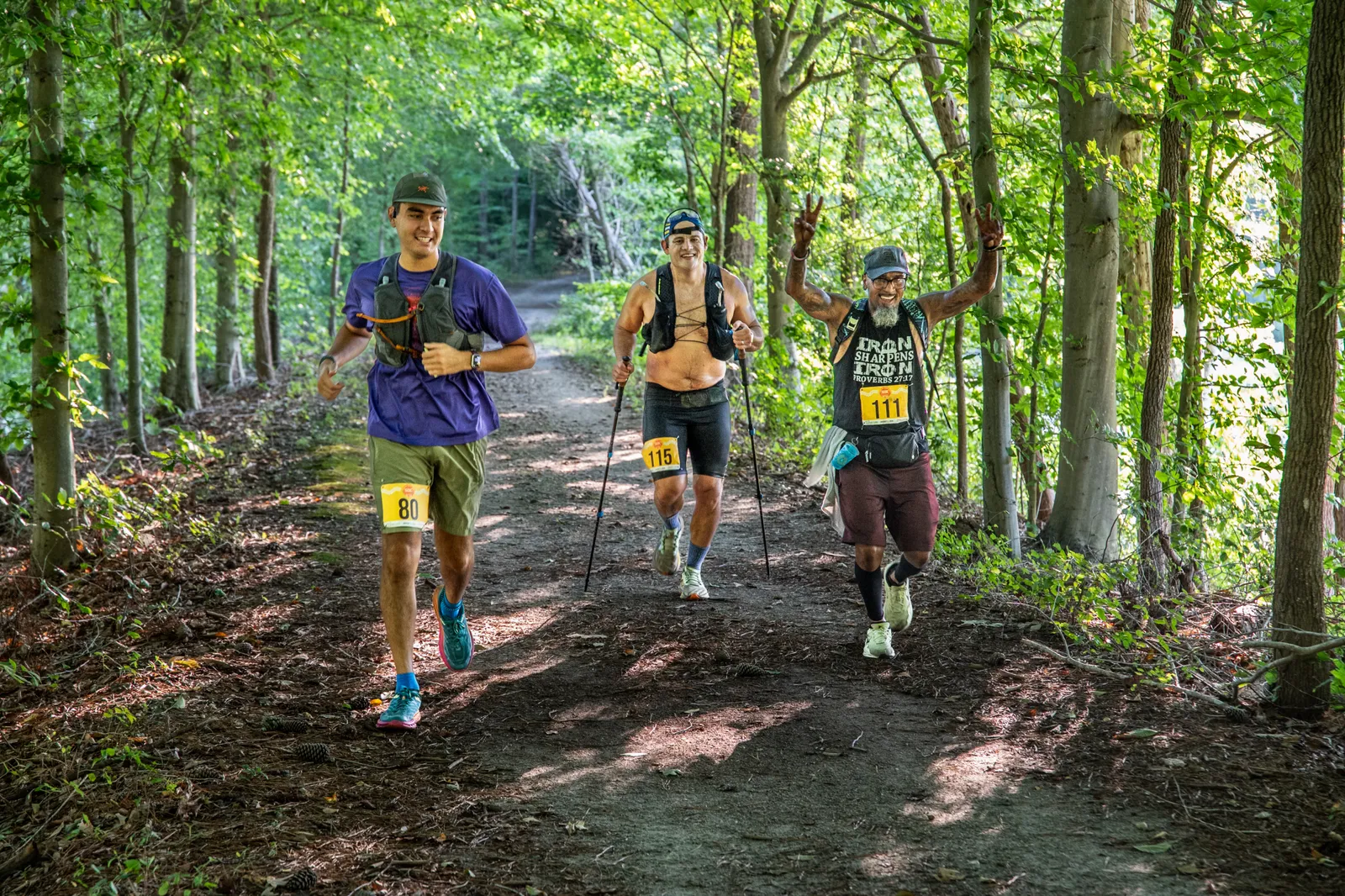 Three runners on a wooded trail, one giving a peace sign.