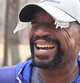 A runner laughs with ice on his cap and eyelashes, indicating cold weather conditions.