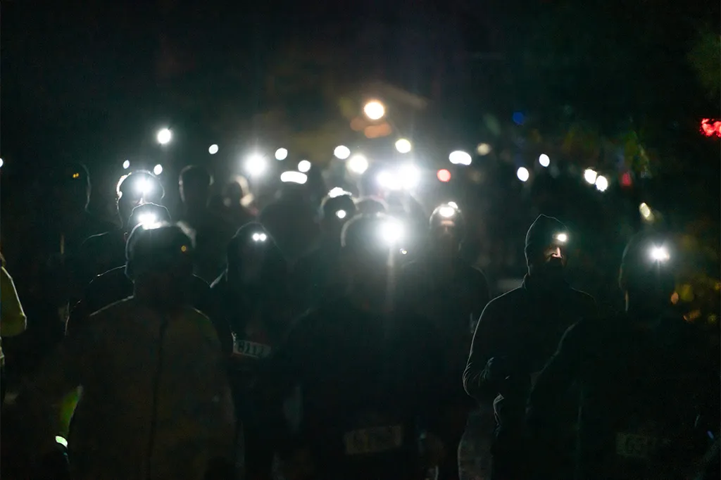 A group of runners at night wearing headlamps, illuminating the trail ahead.