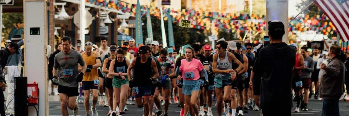 Runners at the start line of a race, with colorful decorations and an American flag in the background.