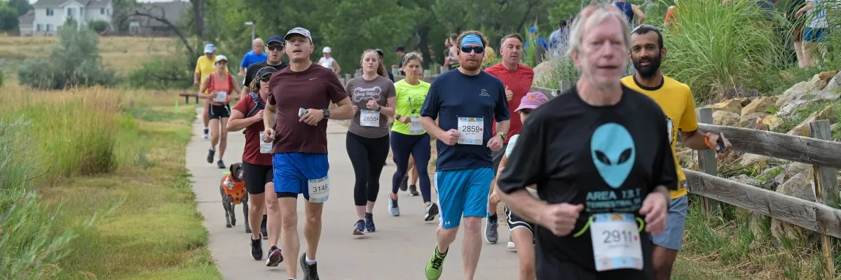 A group of runners on a paved path, with one runner in the foreground wearing a black t-shirt with an alien graphic.