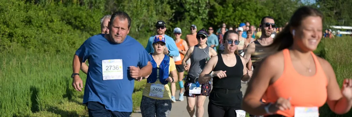 A group of runners participating in a race, with some in the foreground and others in the background, on a paved path surrounded by greenery.