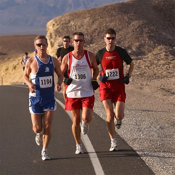 Three male runners in racing bibs running on a paved road with a barren, hilly landscape in the background.