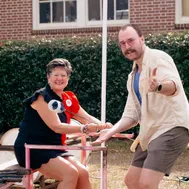 A woman and a man smiling and shaking hands, with the man giving a thumbs-up.