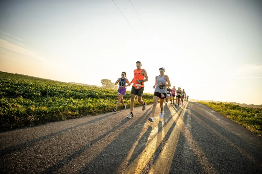 Runners on a road with fields on the side during sunrise.