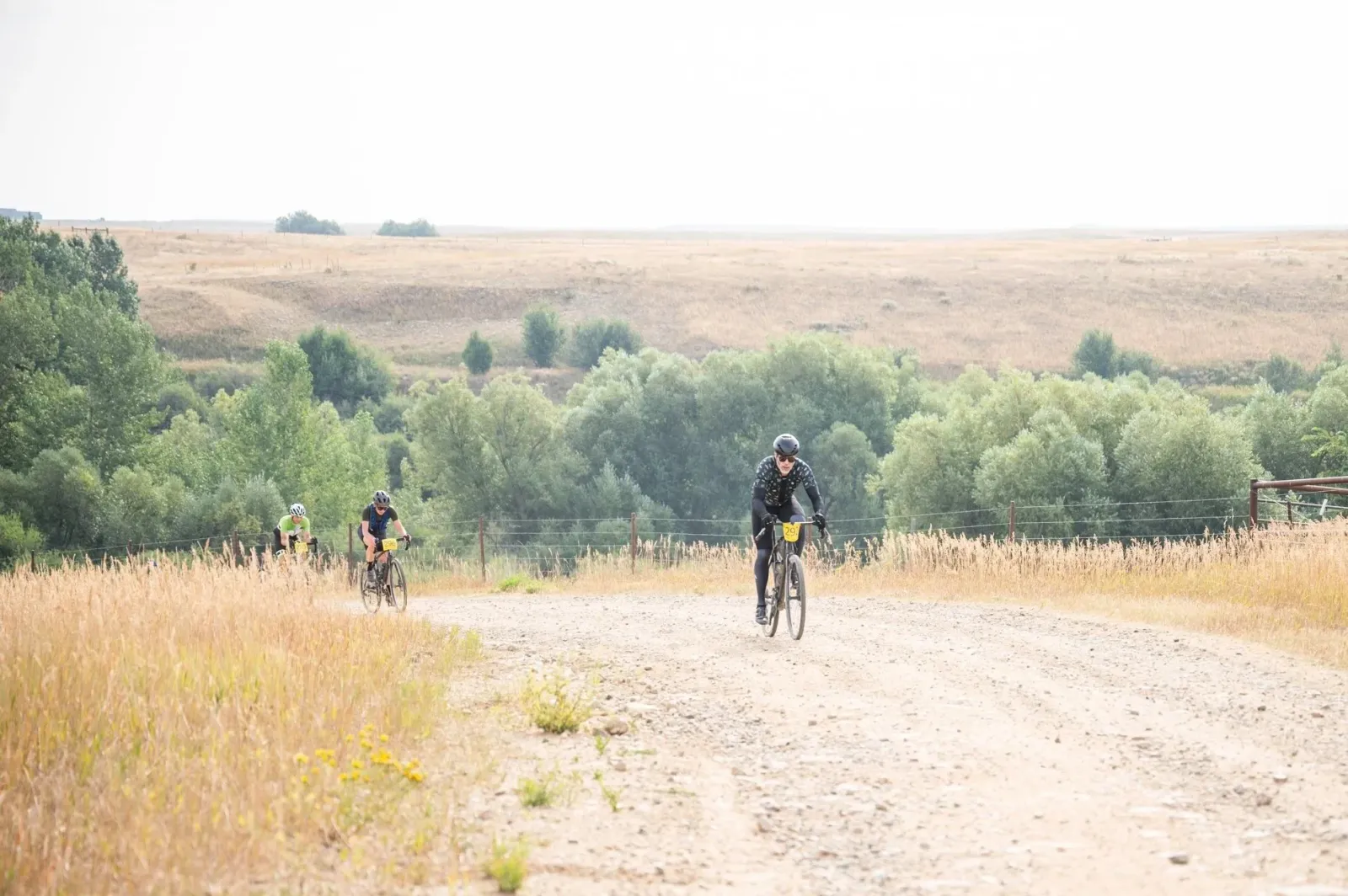 Cyclists riding on a dirt road through a rural landscape.