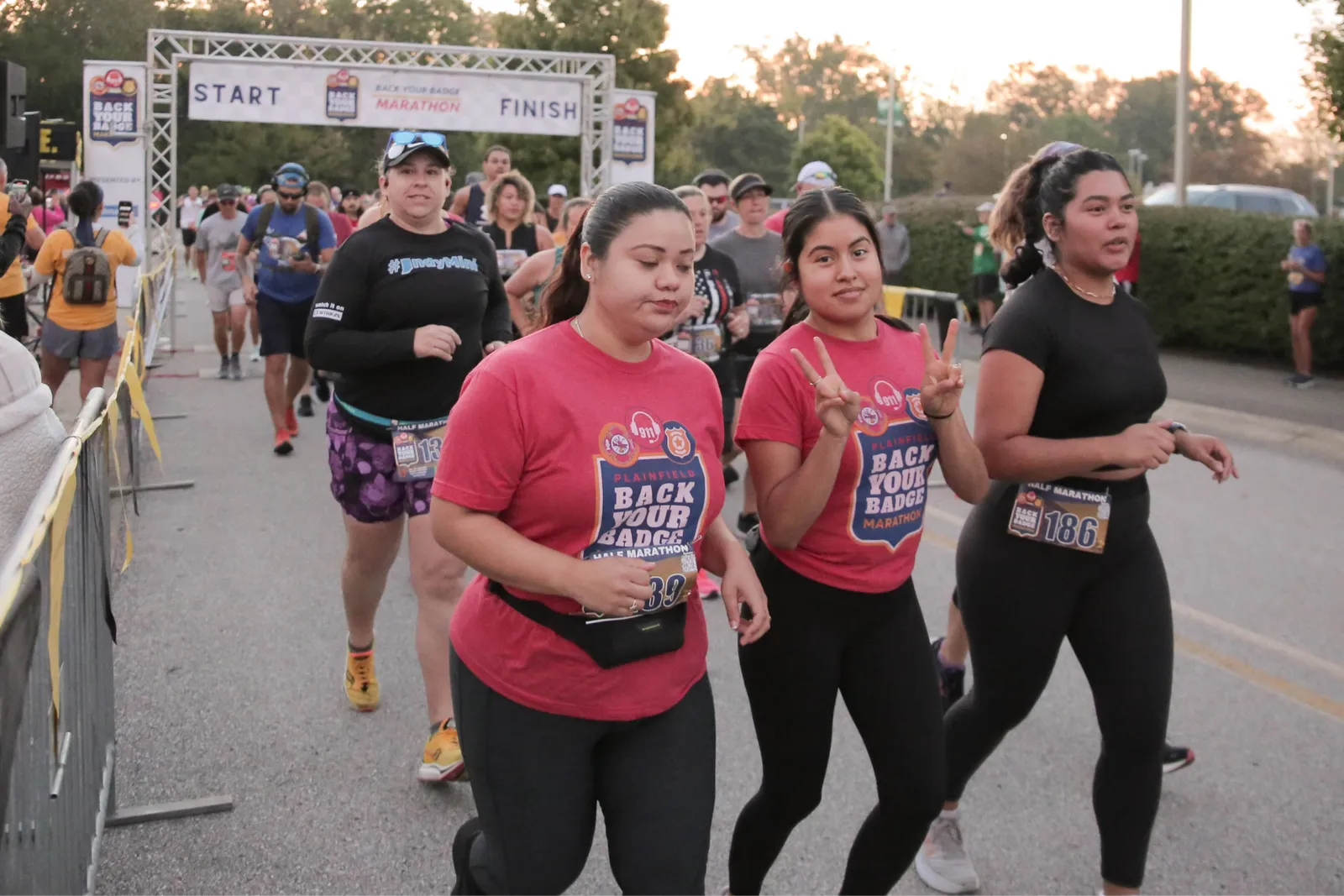 Runners starting the Back Your Badge Marathon, with some in the foreground wearing race t-shirts and bibs.