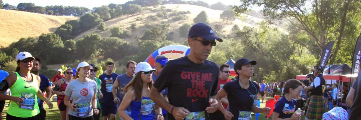 Runners starting a race with a scenic hill in the background and a start line arch.