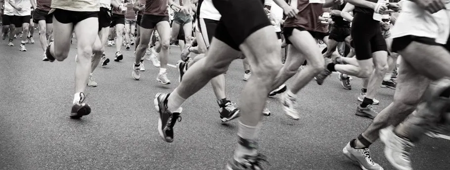 A group of runners' legs and feet as they run on a paved road during a race.