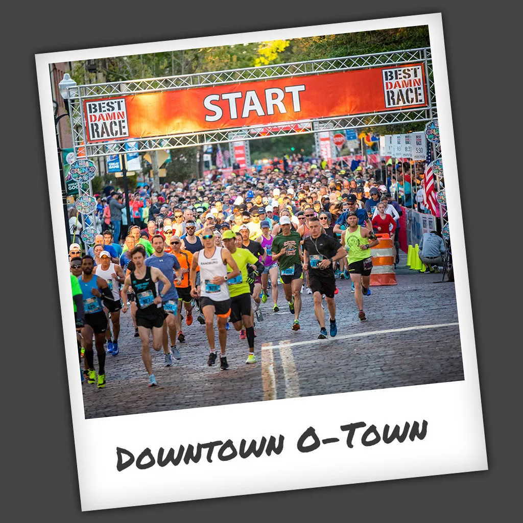 A large group of runners starting a race under a banner that says 'START' and 'BEST DAMN RACE'.