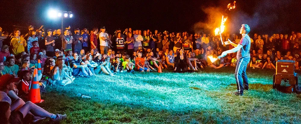 A crowd of people watching a fire performer at night.
