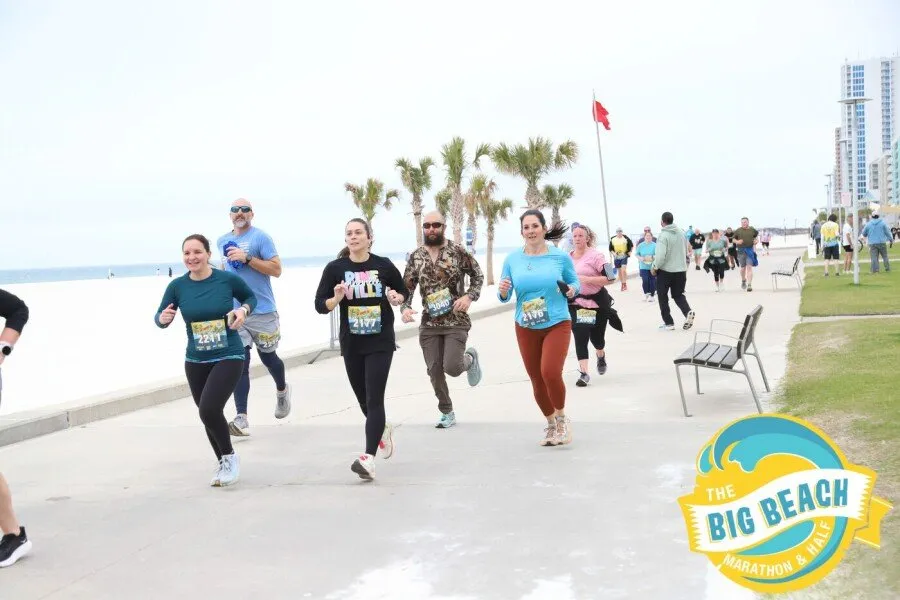 Runners participating in the Big Beach Marathon & Half Marathon along a paved path with the beach and ocean in the background.