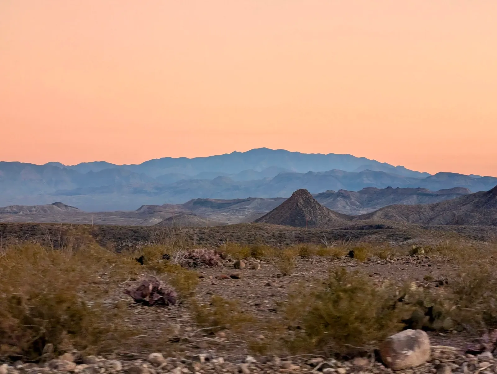 Desert landscape with layered mountains under a pink sky.