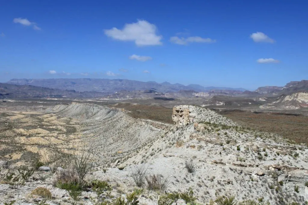 Scenic view of rugged desert mountains and valleys under a blue sky with scattered clouds.