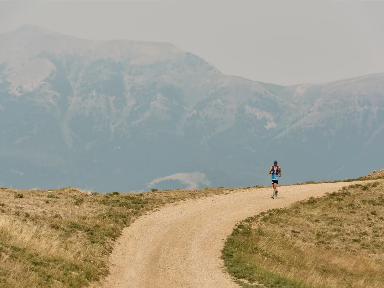 A solo runner on a dusty, winding trail with mountains in the background.