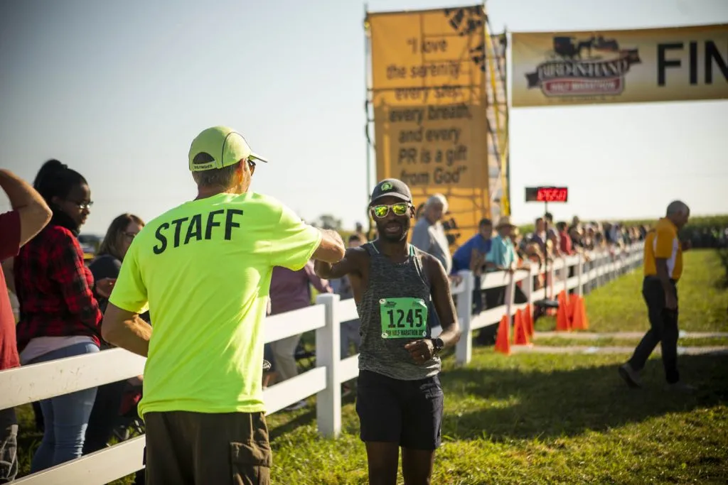 A runner smiles and gives a fist bump to a staff member near the finish line of the Bird-in-Hand Half Marathon.