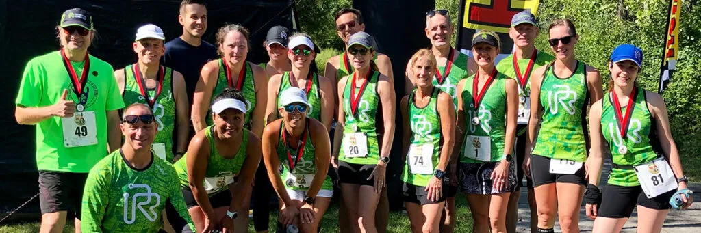A group of runners, some wearing green shirts and medals, pose for a photo after completing a race.