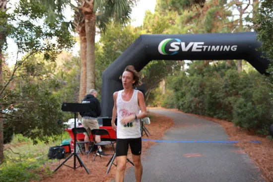 A runner wearing a white tank top and black shorts runs towards an inflatable archway with 'SVETIMING' printed on it.