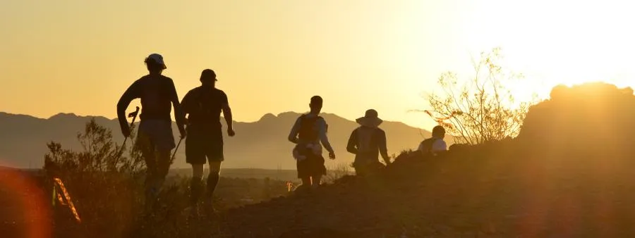 Runners on a trail at sunset with mountains in the background.