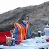 A person wearing a safety vest and mask stands behind a table at a race aid station.