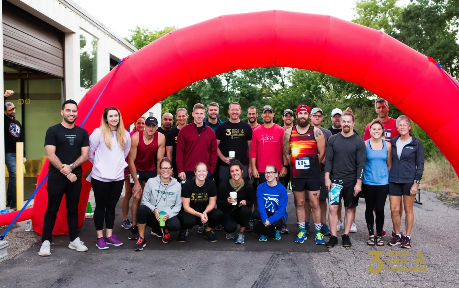 A group of runners pose for a photo under a large red inflatable arch at the start line of a race.