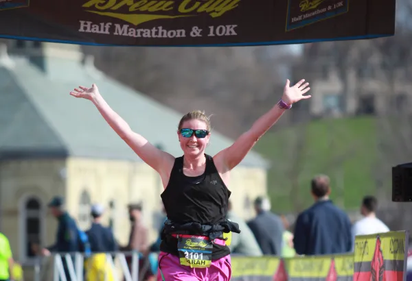 A female runner with arms raised in celebration crosses the finish line of the Brew City Half Marathon.