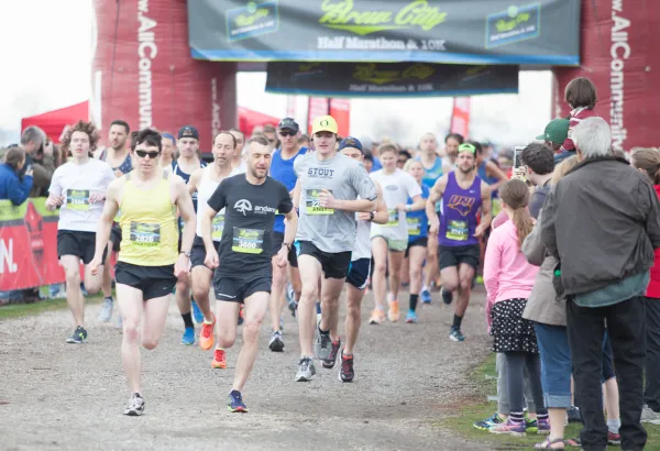 Runners starting the Brew City Half Marathon, 10K, and 5K races under a large archway.