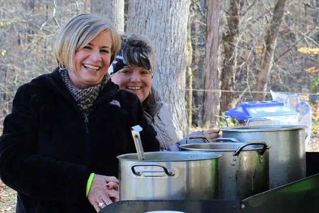 Two smiling women standing behind large cooking pots, possibly volunteers at a race event.