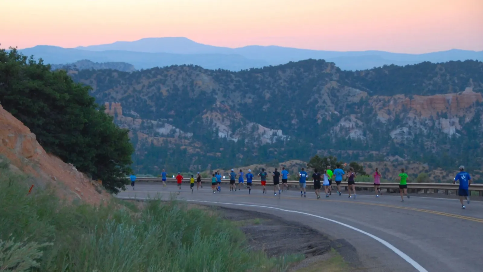 Runners on a road with scenic mountains in the background at sunrise.
