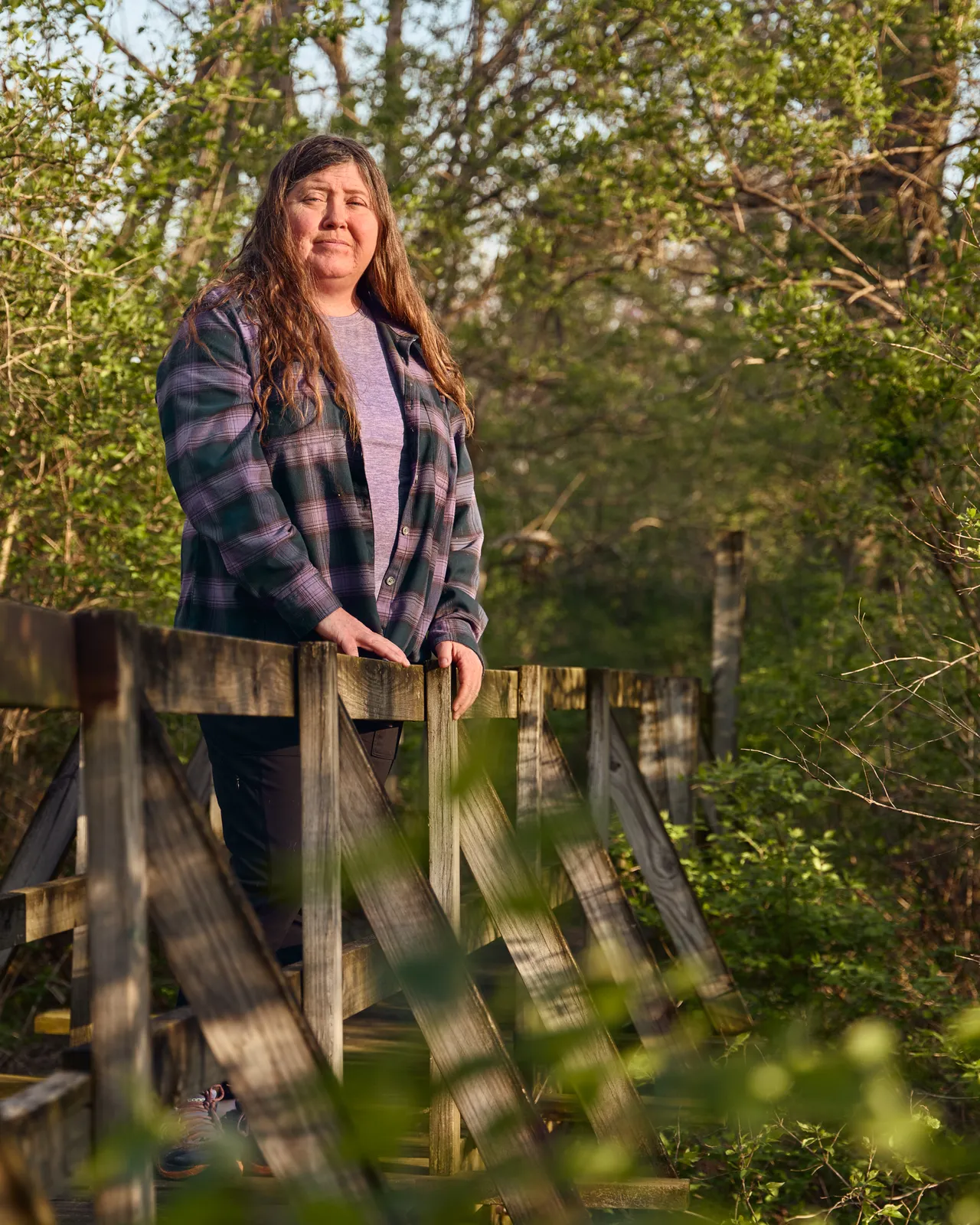 A woman stands on a wooden bridge on a wooded trail.