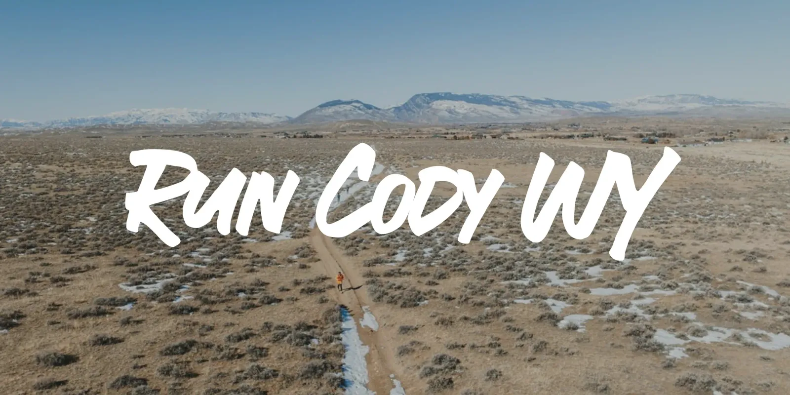 A lone runner on a dirt path with mountains in the background and the text 'Run Cody WY' overlaid.