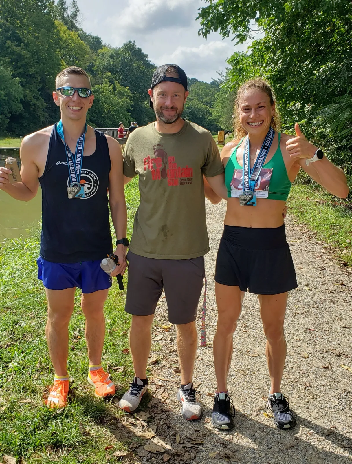 Three people, two of whom are runners wearing medals, smiling and posing for a photo after a race.