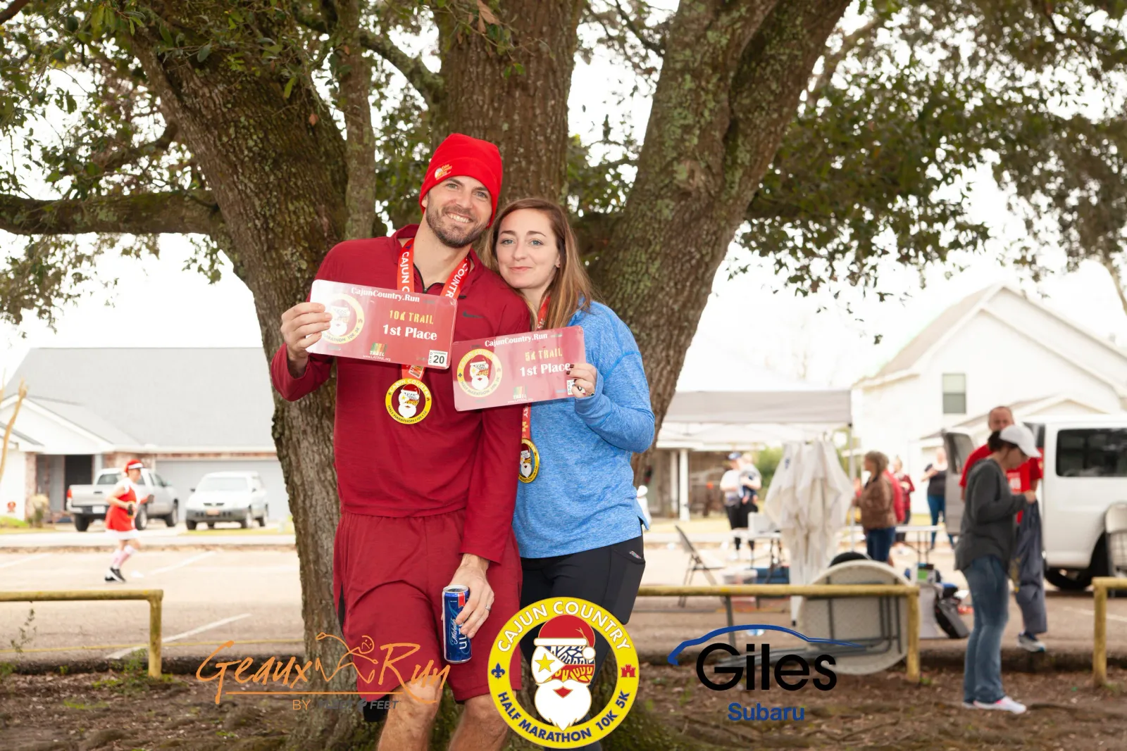 A smiling couple poses for a photo, holding race awards and wearing medals from the Cajun Country Run.