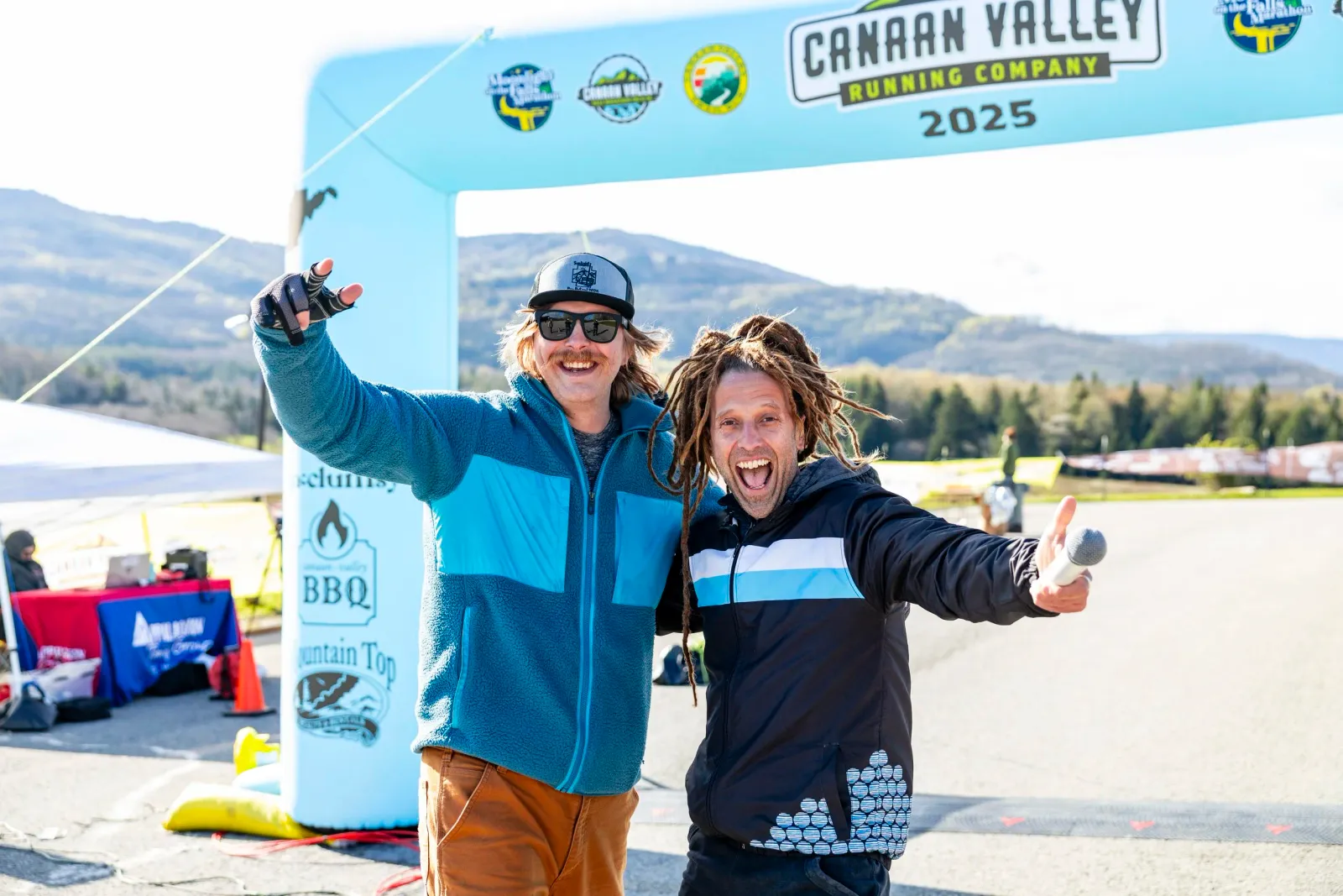 Two men celebrating at the Canaan Valley Running Company arch, one holding a microphone.