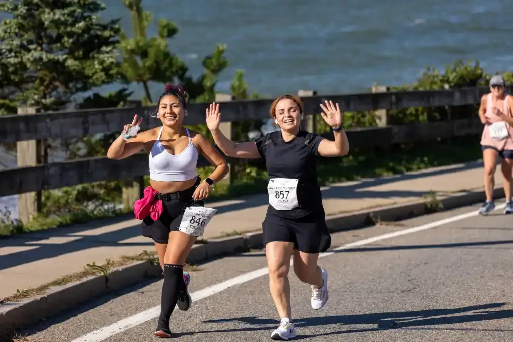 Two women running and smiling, with the ocean in the background.