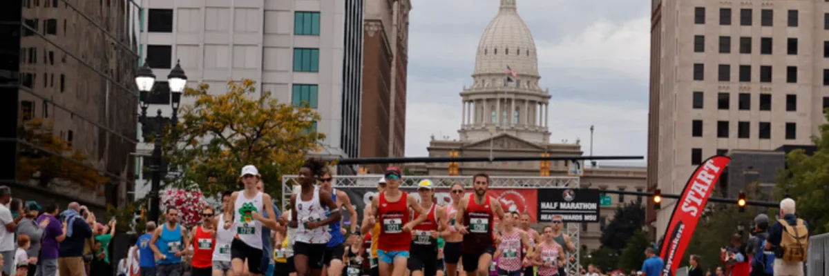 Runners at the start line of the Capital City River Run with the Michigan State Capitol building in the background.