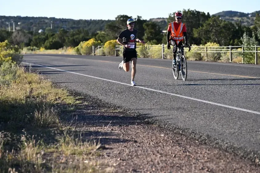 A runner on a road with a cyclist in the background.