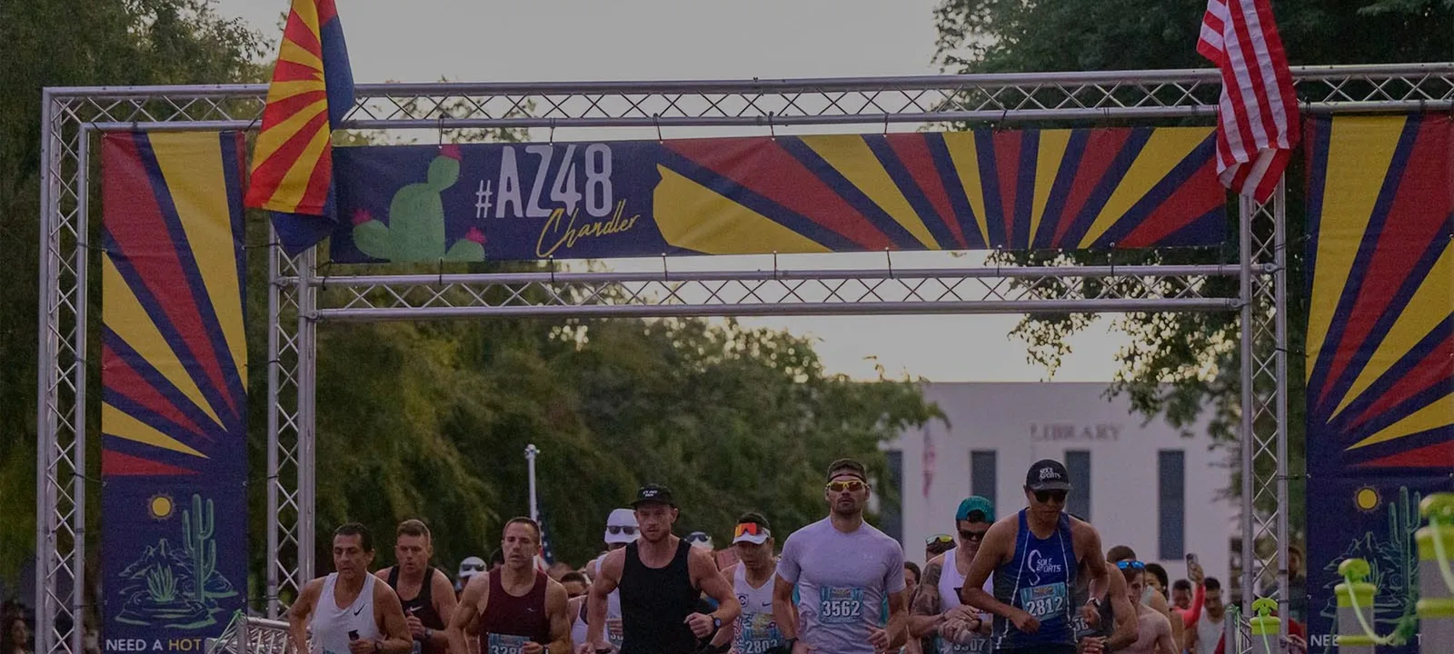 Runners at the start line of the AZ48 Chandler Half Marathon & 5K, with race banners and flags overhead.