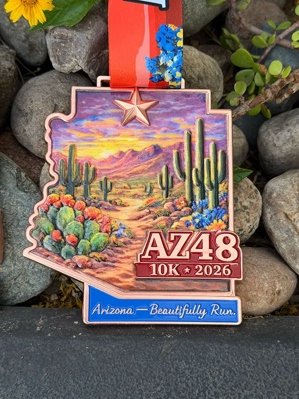 Arizona 48 10K 2026 medal featuring a desert landscape with saguaro cacti and a sunset, with the text "Arizona - Beautifully Run."