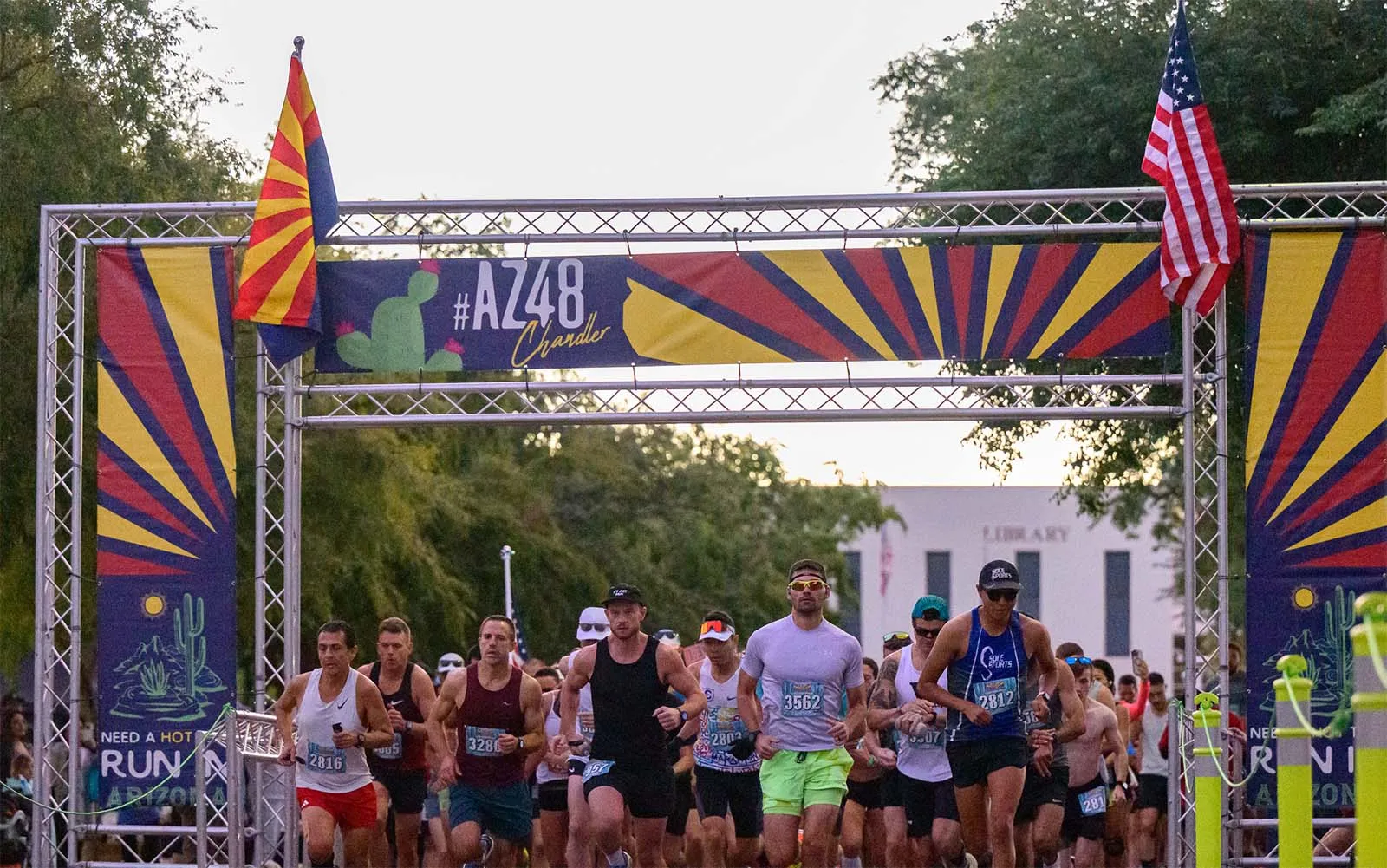 Runners crossing the start line at the AZ48 Chandler Half Marathon & 5K, with Arizona flags and race banners overhead.