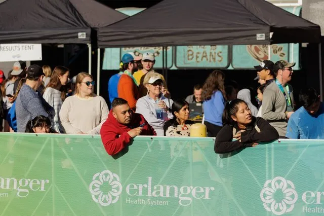 Spectators watch a race from behind a green barrier with sponsor logos.