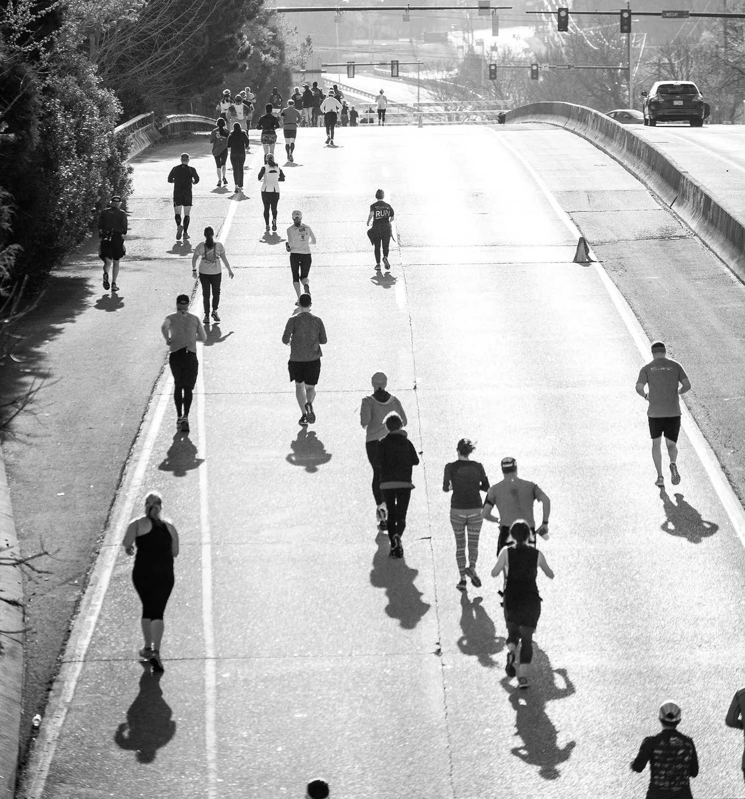 Runners on a road course, seen from above, with long shadows cast by the sun.