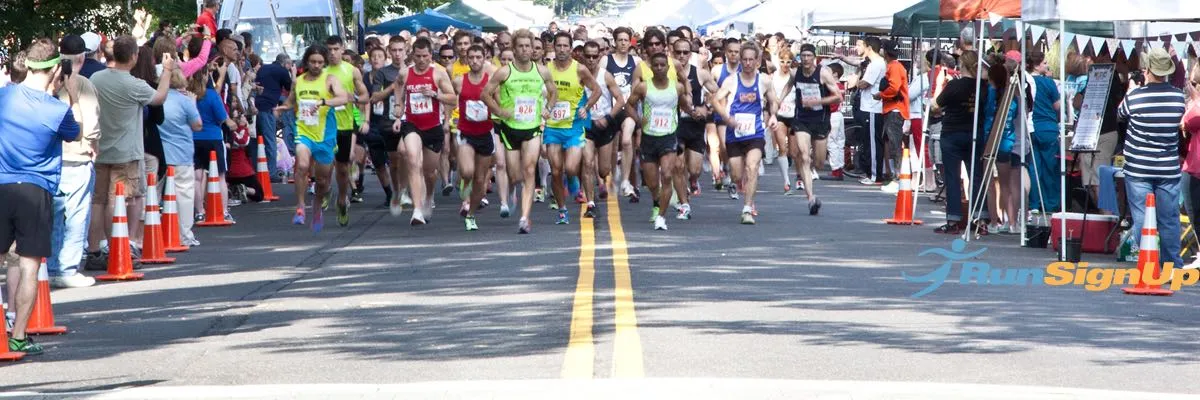 A large group of runners starting a race on a paved road, with spectators lining the sides.